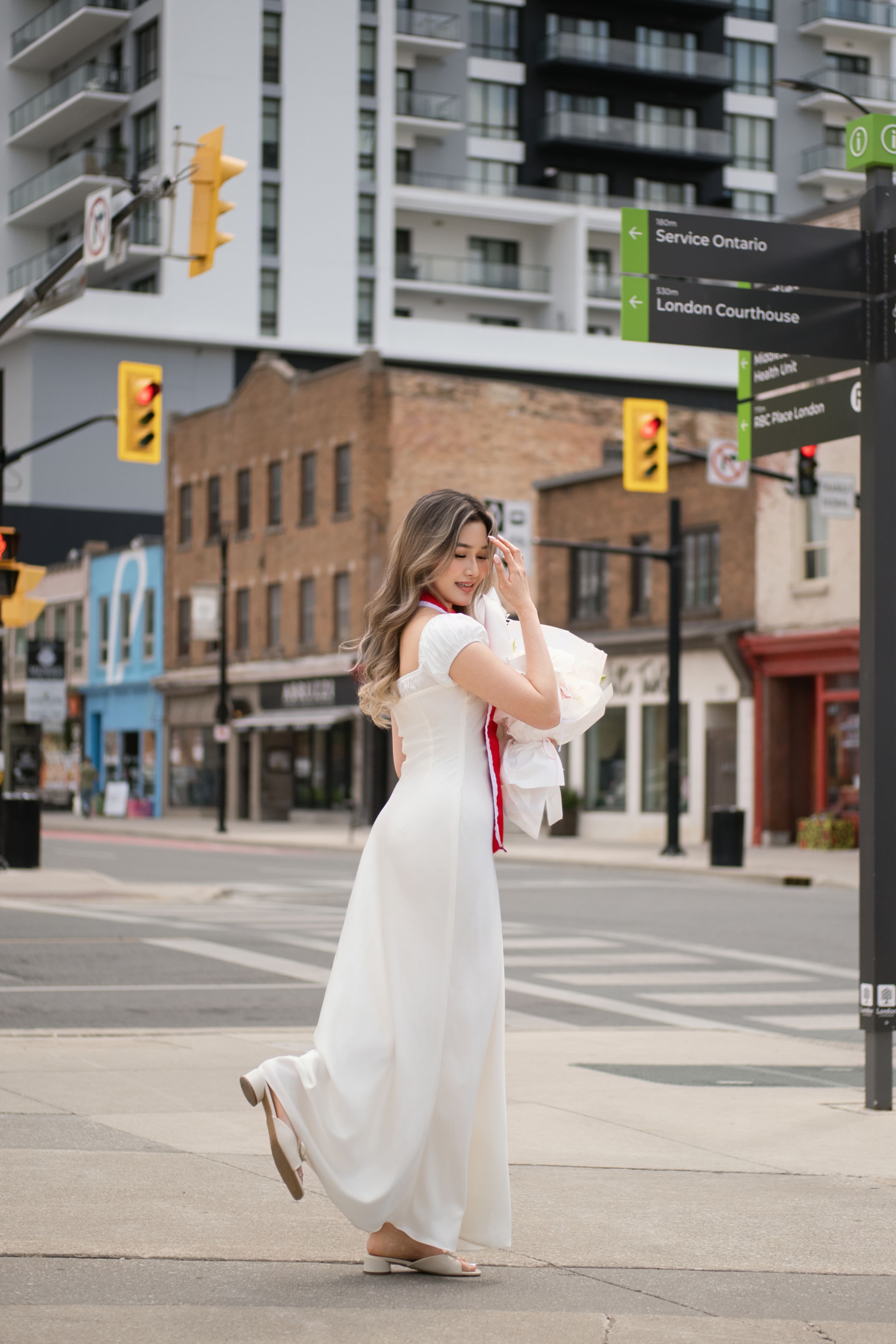 Candid graduation portrait of a Fanshawe College graduate walking across a downtown street in London, Ontario while carrying flower bouquets.