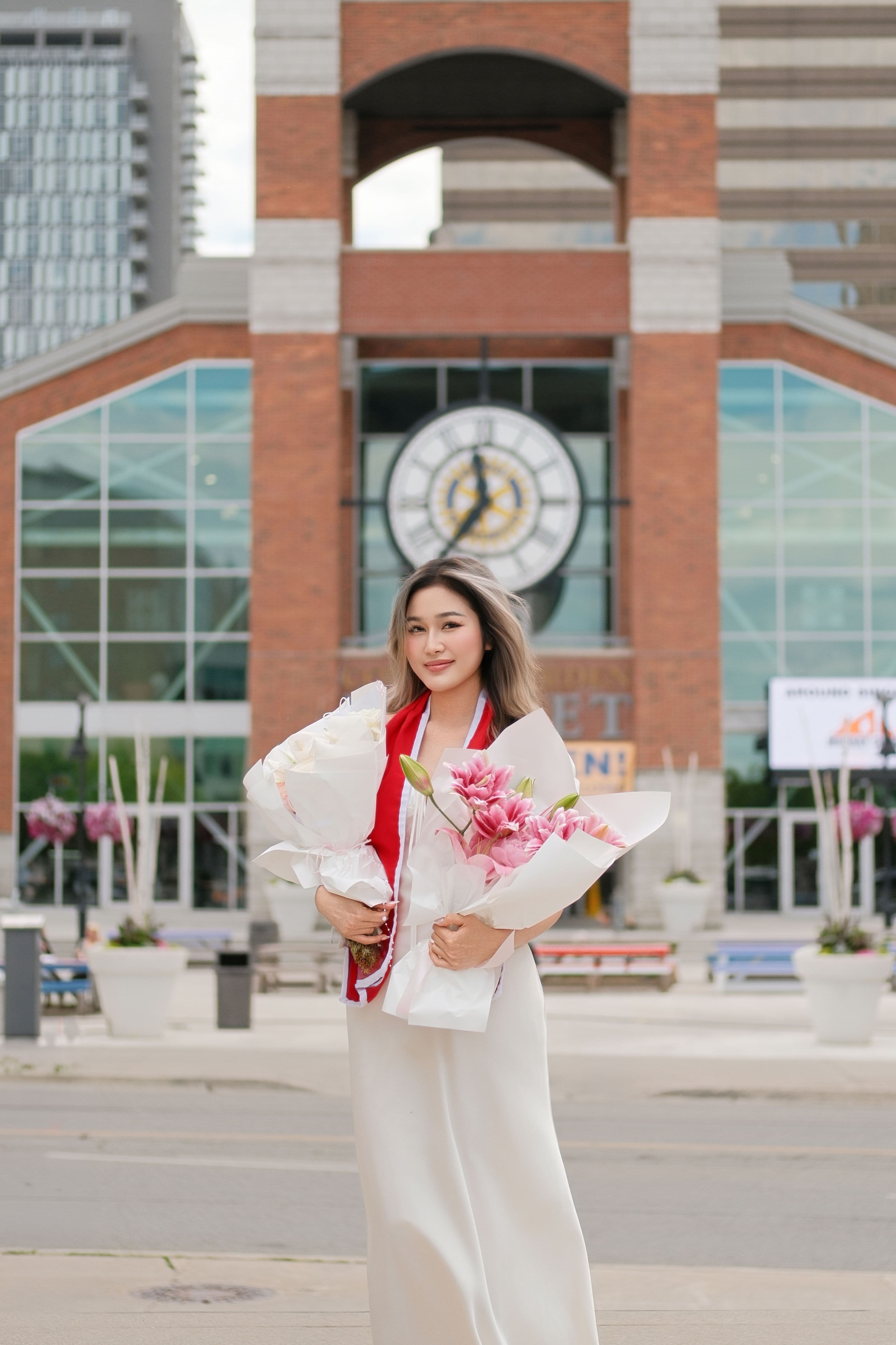 Portrait of a Fanshawe College graduate posing with flower bouquets in front of Covent Garden Market in London, Ontario.