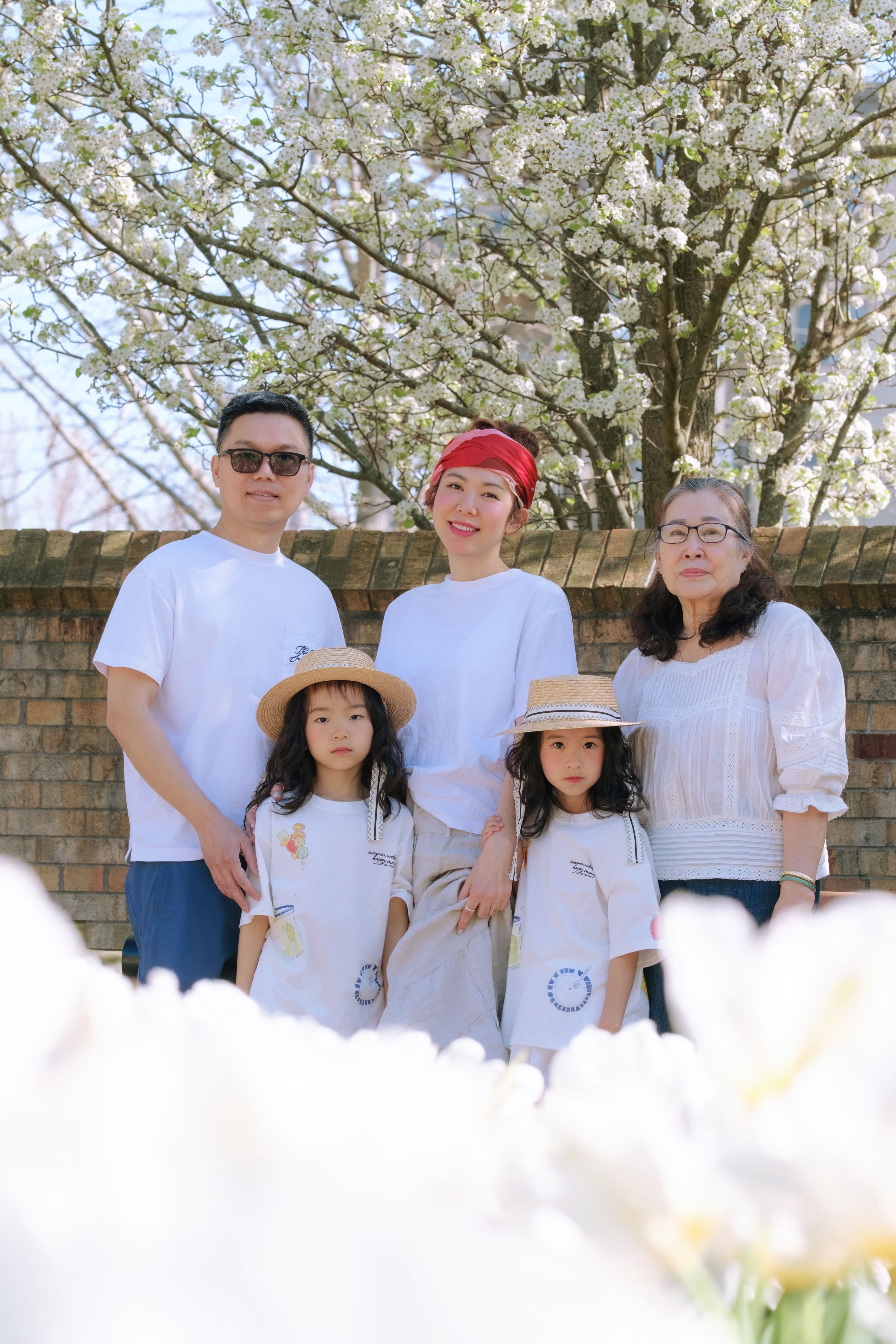 Three generations of a family in matching white outfits posing under blossoming trees.