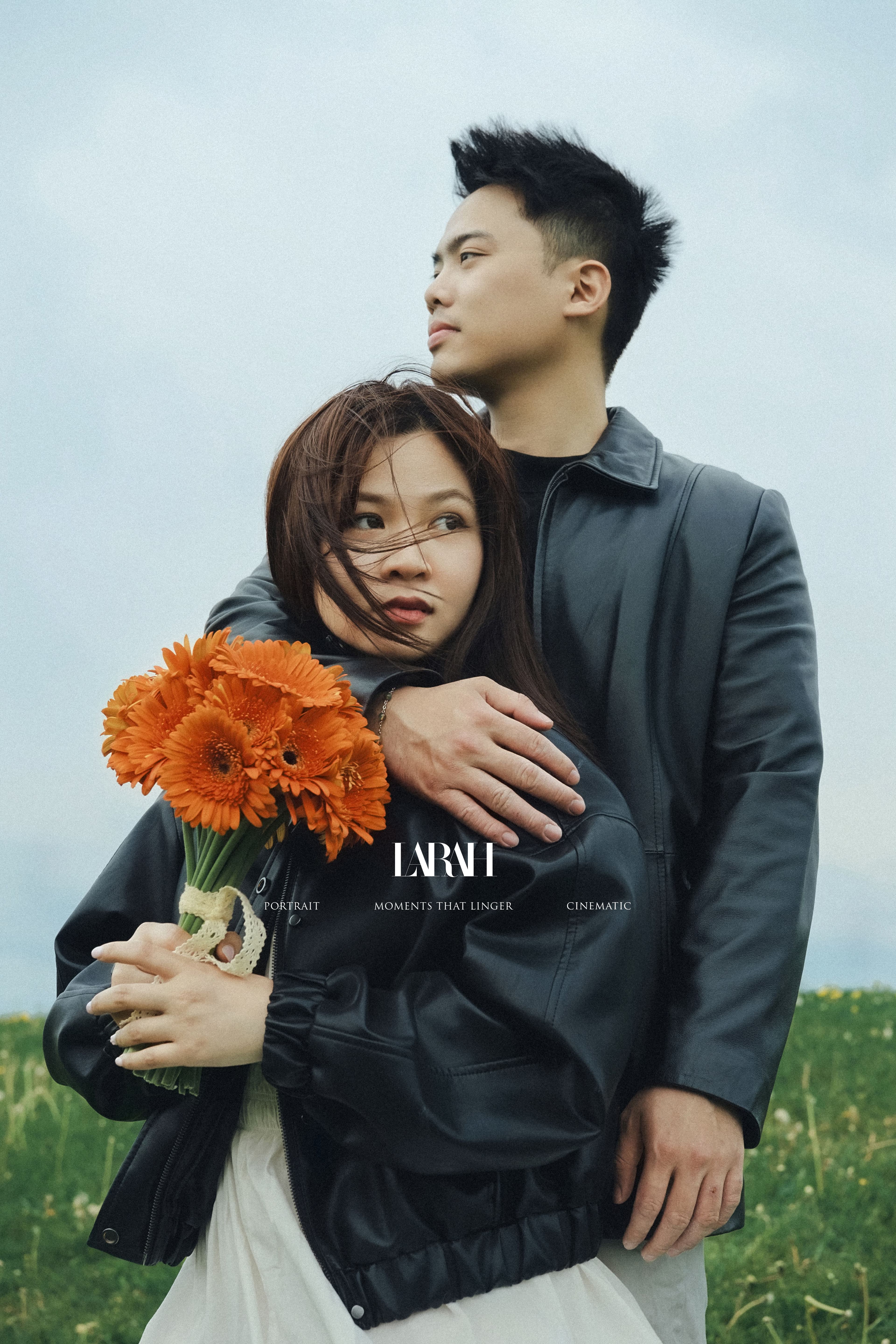 Couple hugging outdoors while holding a bouquet of orange gerbera daisies.