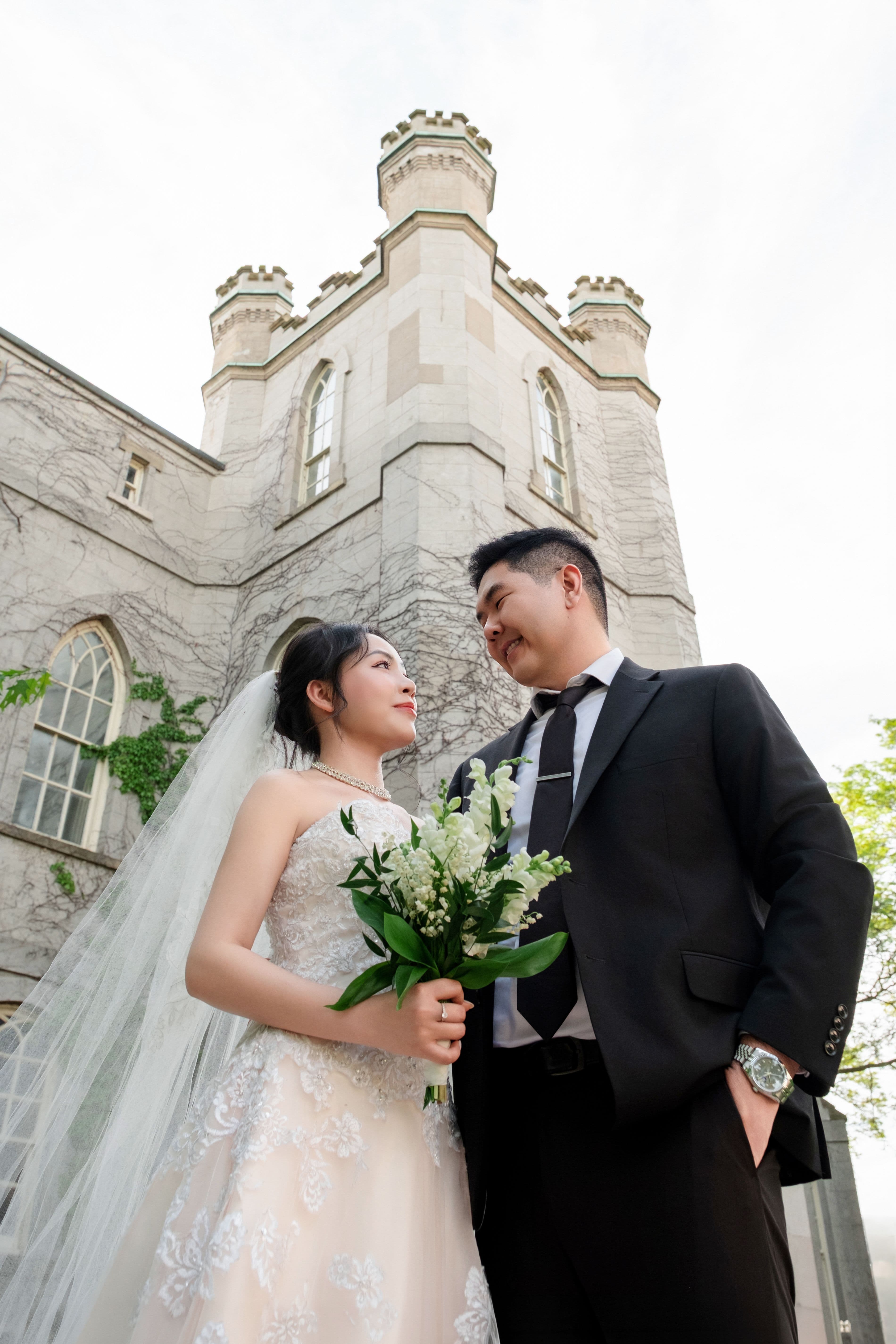Close portrait of a bride and groom smiling at each other with the castle tower behind them.
