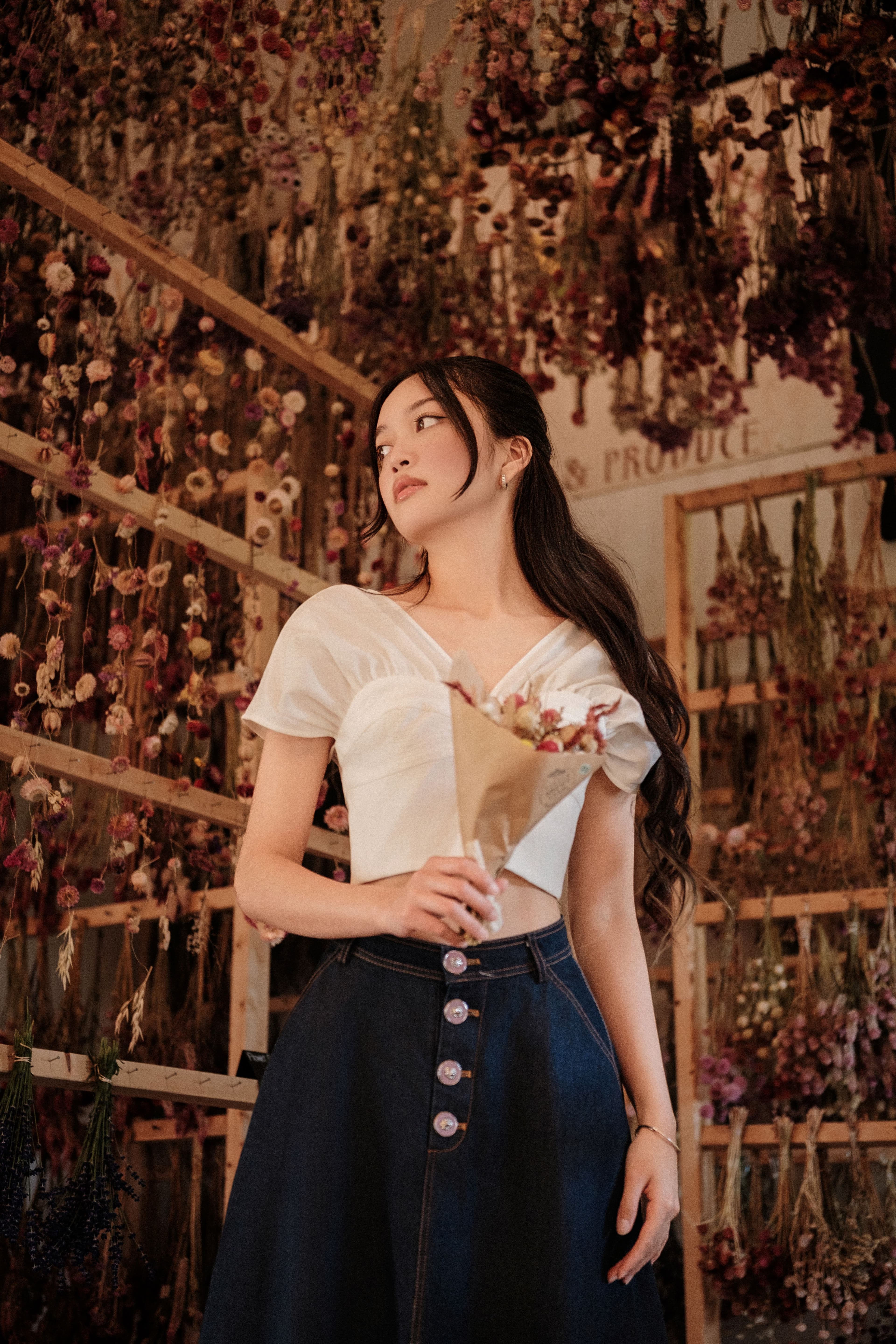Woman standing beneath a ceiling of hanging dried flowers inside the shop.