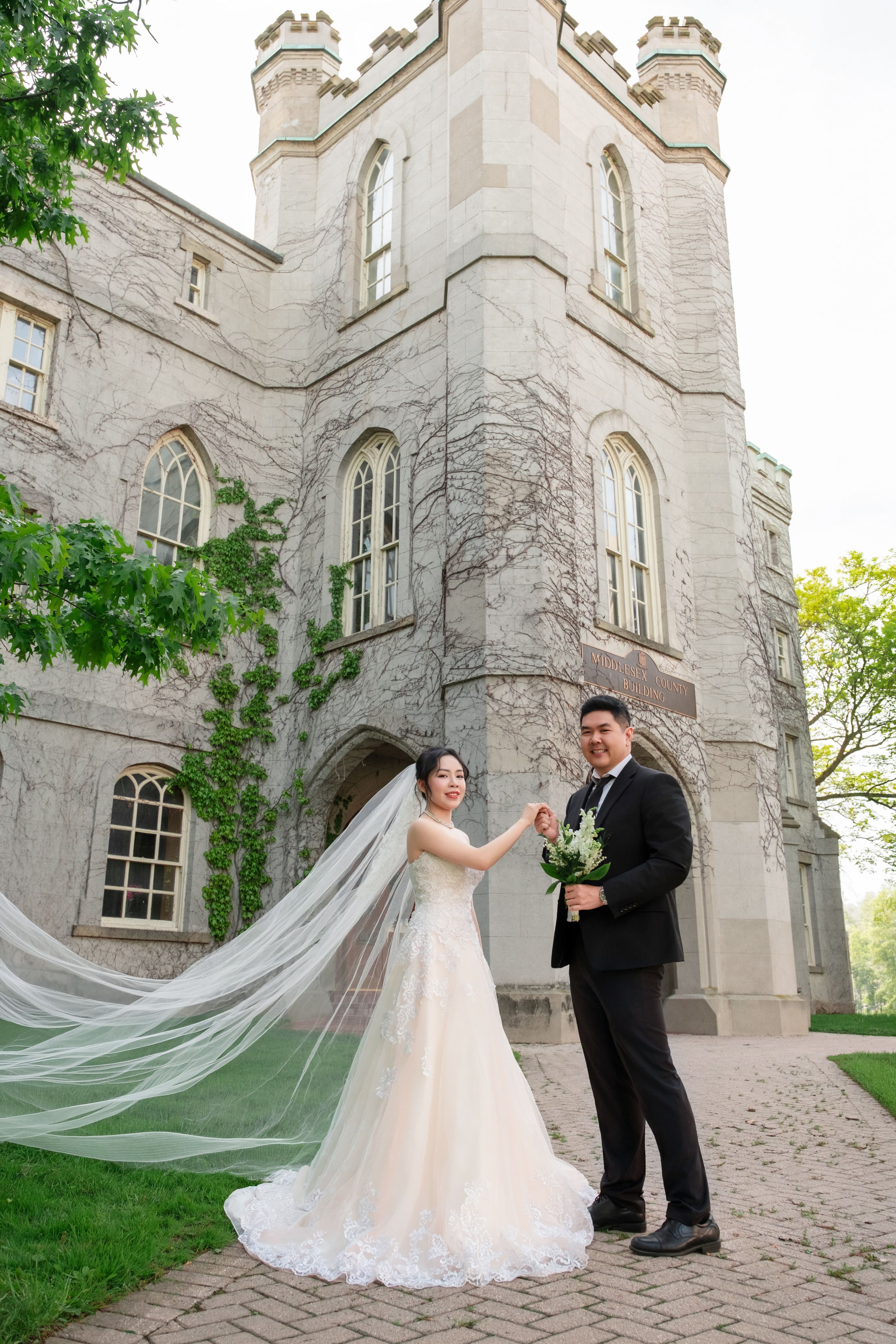 Bride with a long cathedral veil reaching toward the groom on the castle grounds.