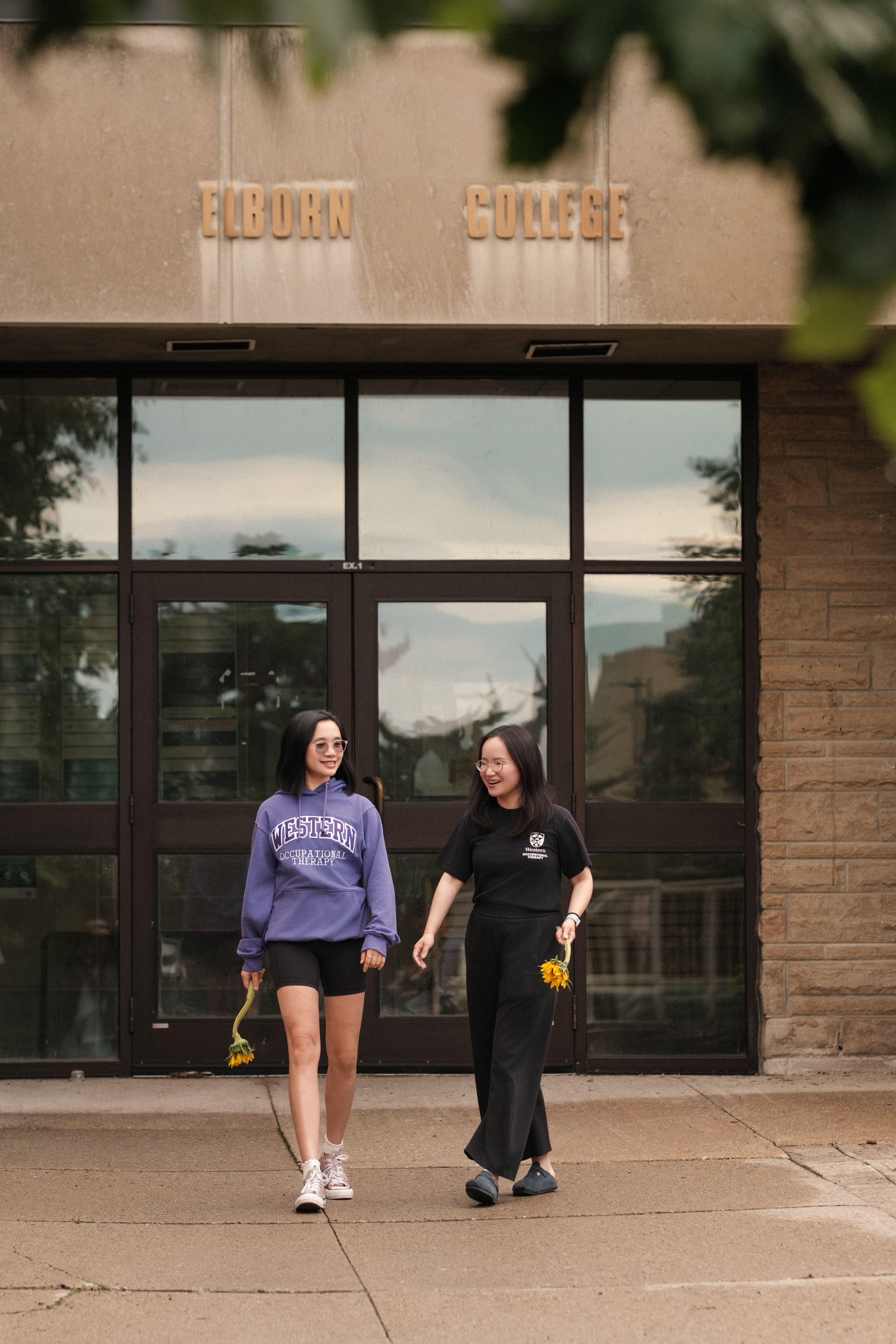 Two friends walking together in front of the Elborn College entrance at Western University.